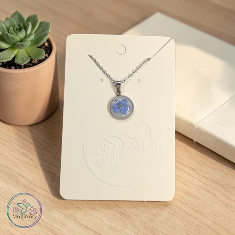 Okrągły wisiorek z niezapominajką na mlecznobiałym tle